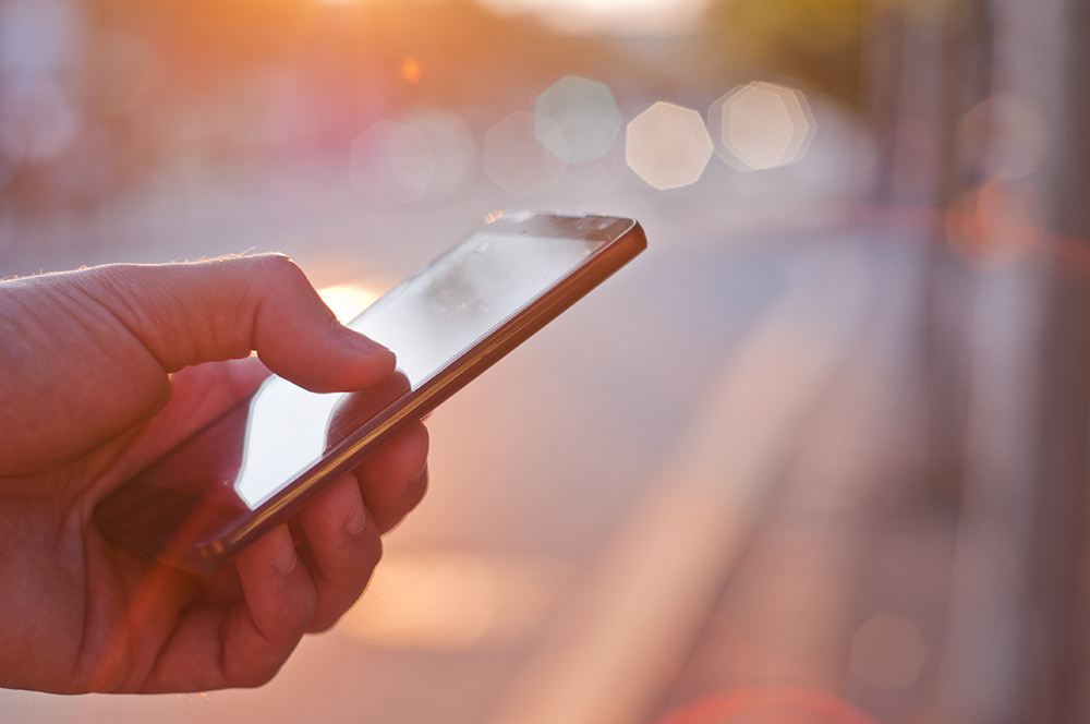 hand holding a smart phone with a blurry street in the background