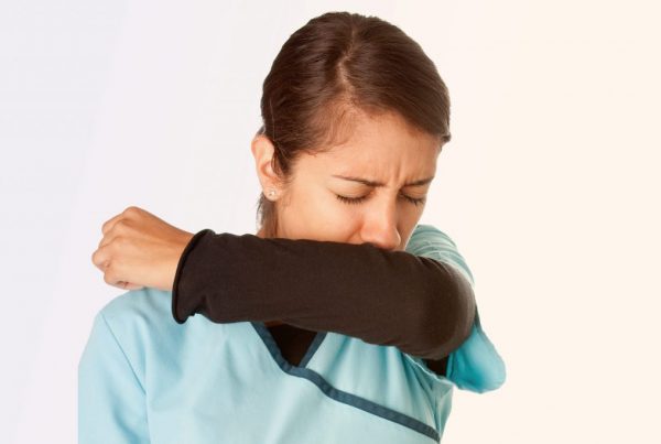 person wearing scrubs coughing into elbow