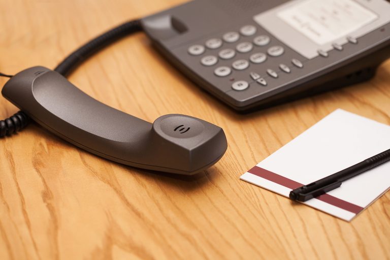 an office phone off the hook, with a pen and pad of paper next to it