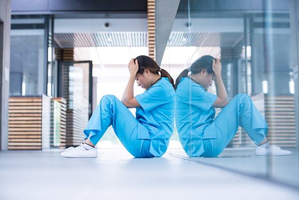 Woman in scrubs sitting on the floorwith her head in her hands