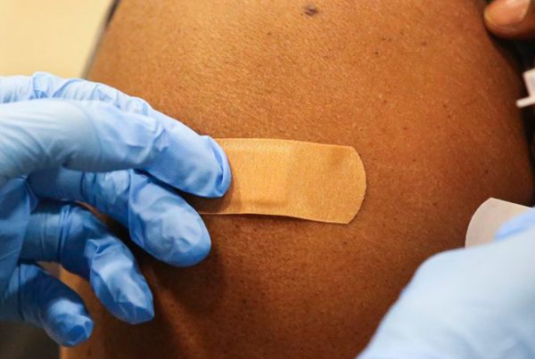 gloved hands putting a bandaid on a person's shoulder