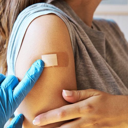 a gloved hand adjusts a bandaid on a person's shoulder