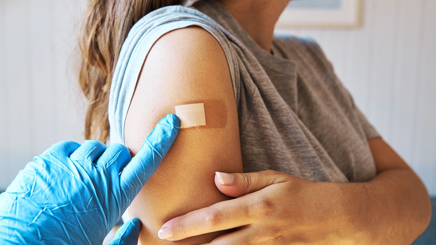 a gloved hand adjusts a bandaid on a person's shoulder