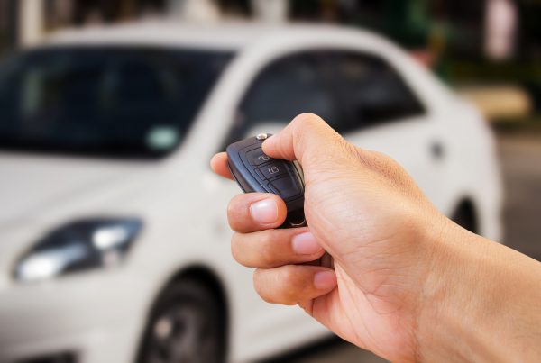 a hand pressing the button of a key fob with a car in the background