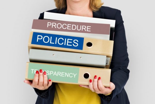 Person holding pile of binders labelled "procedure", "Policy" and "transparency"