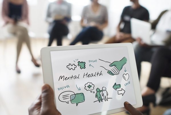 hands holding a sign the reads "mental health" with group of people in the background