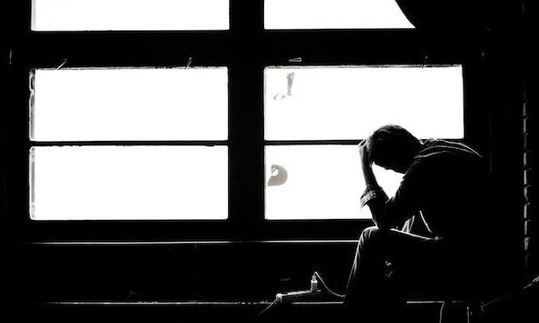 tired or sad person with head in hand silhouetted against a window