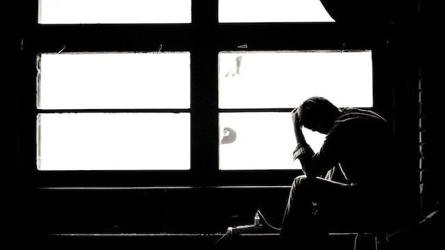 tired or sad person with head in hand silhouetted against a window