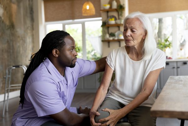 black man with long hair wearing scrubs talks to senior woman