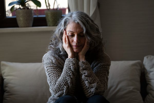 woman with long grey hair sttingon a sofa with her head in her hands