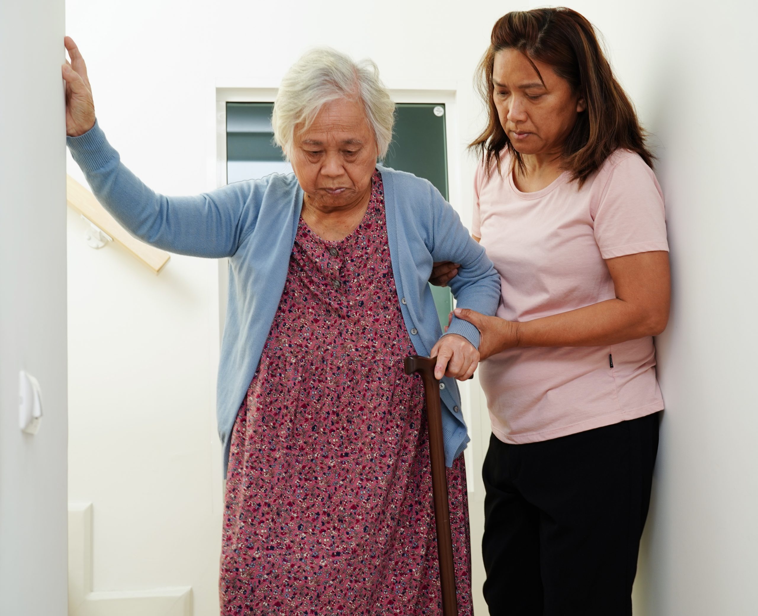 caregiver supporting a senior walking down stairs with a cane