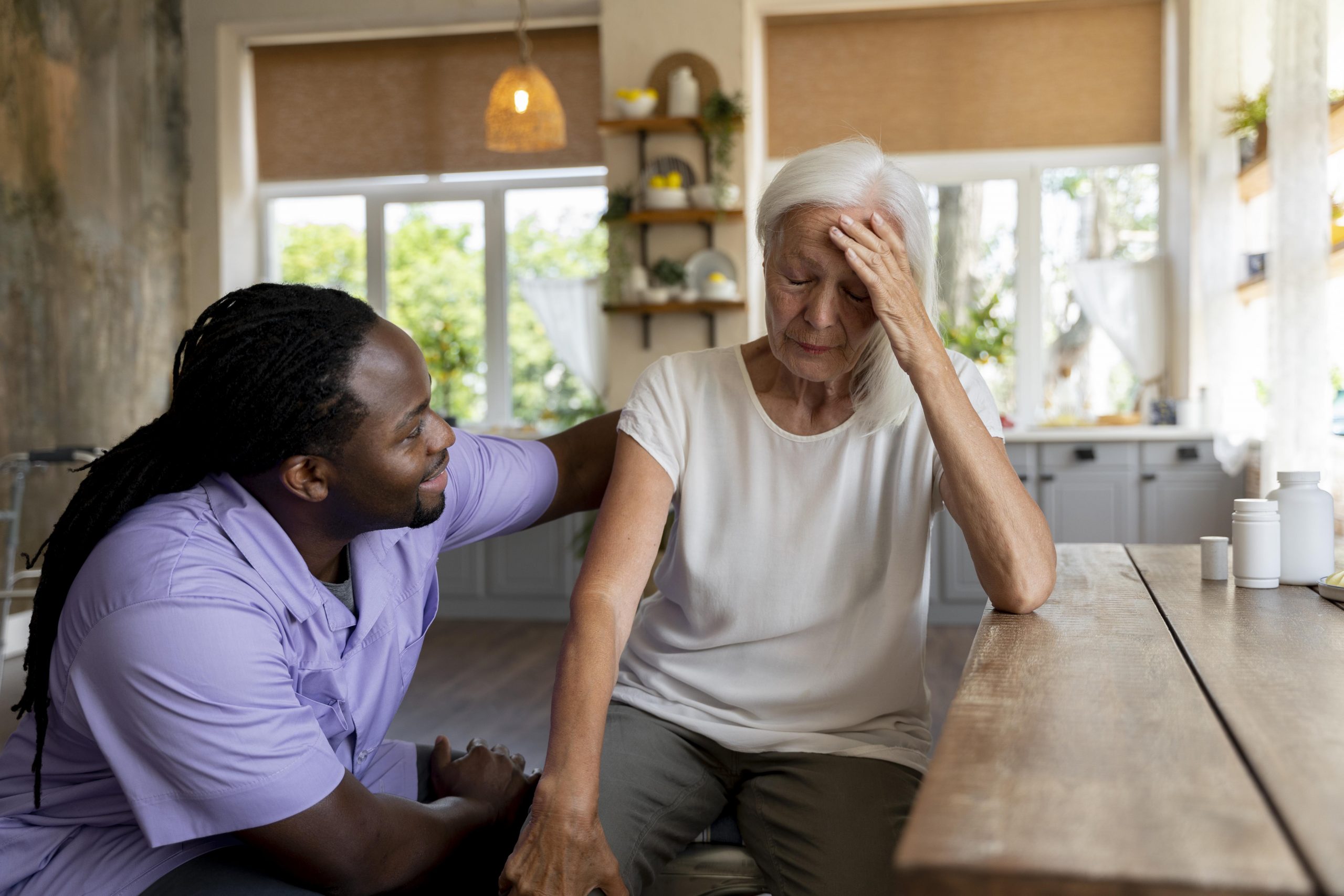 Black man in scrubs assisting senior woman with her head in her hands