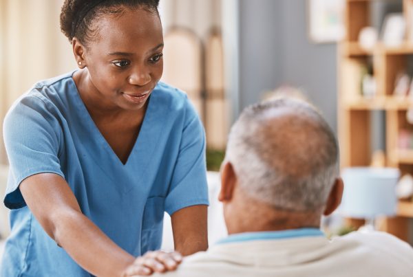 Black woman wearing scrubs touching the shoulder of a senior man