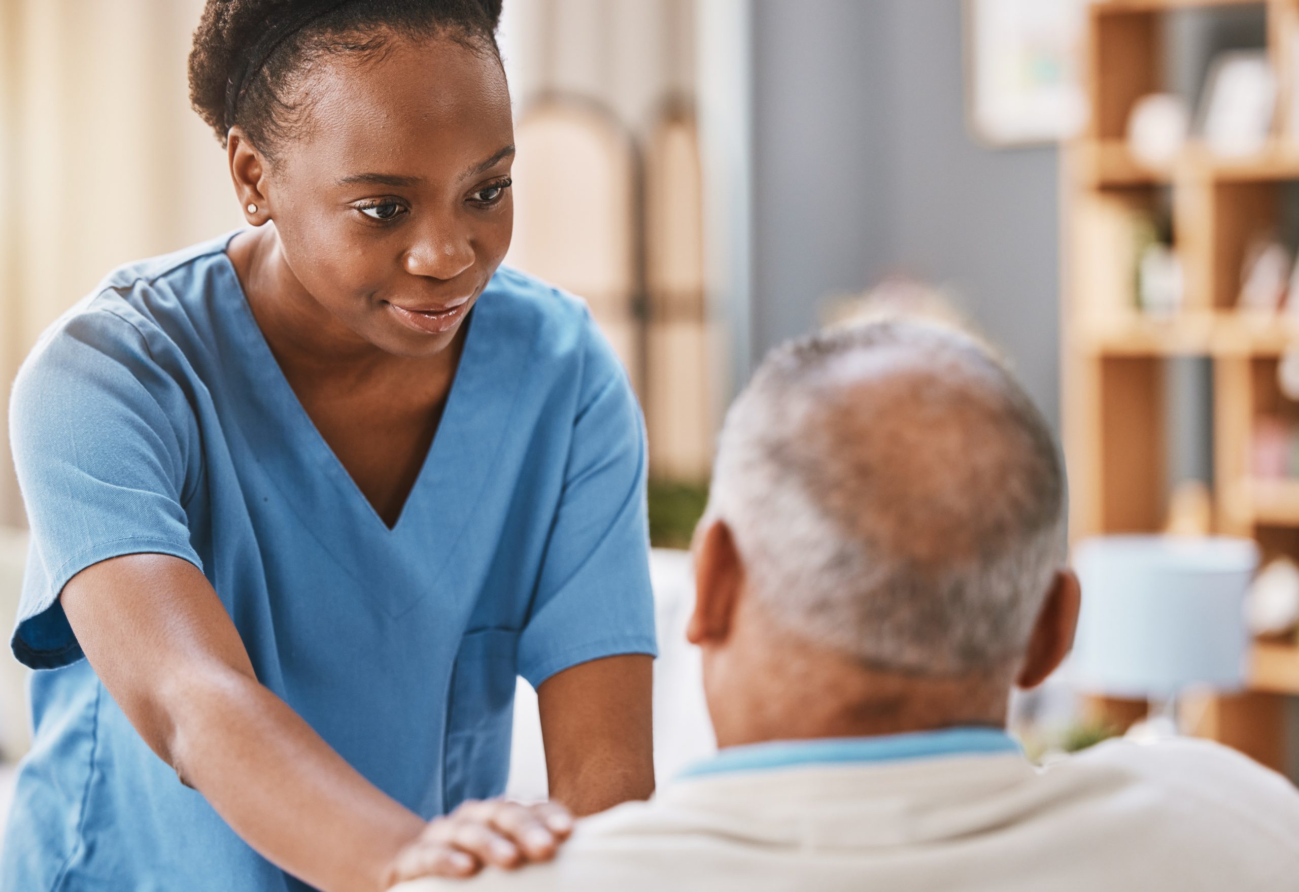 Black woman wearing scrubs touching the shoulder of a senior man