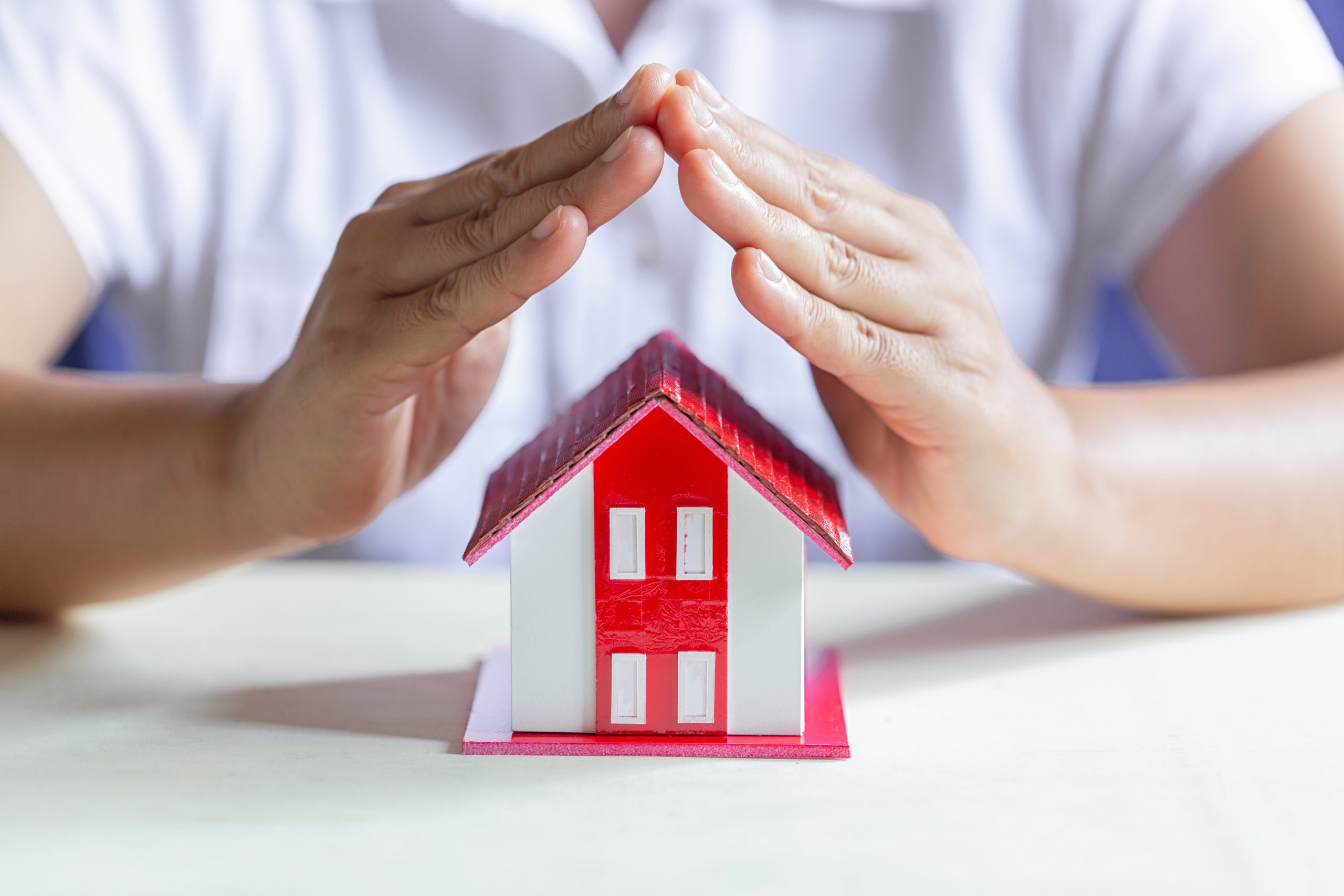 person with hands over the roof of a model house