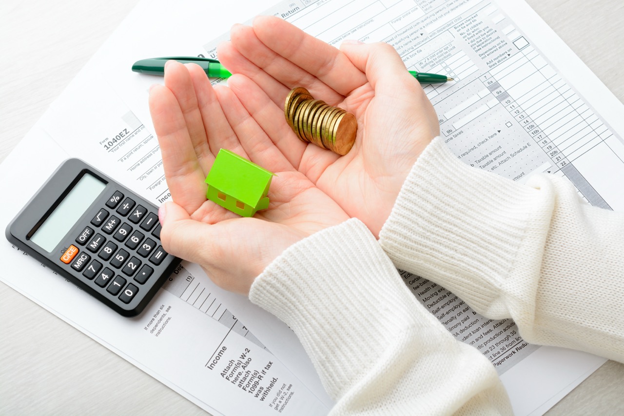 "two hands holding coins and tiny model house over tax documents"