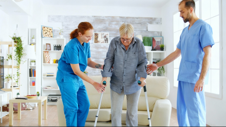 "two workers help senior man walk on his crutches"